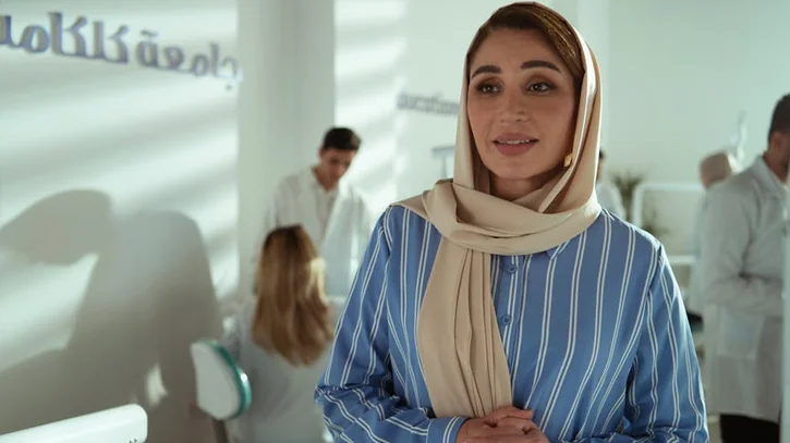 Woman in a striped shirt in an office with colleagues in the background.