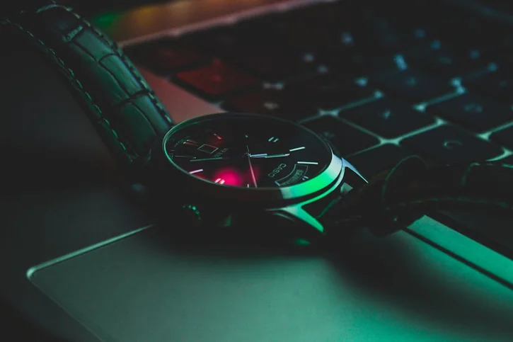 Close-up of a stylish analog wristwatch resting on a laptop keyboard, highlighting luxury and technology.