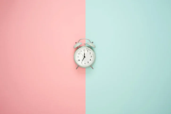 A vintage round clock on a split pastel pink and blue background.