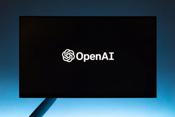 Minimalist display of OpenAI logo on a screen, set against a gradient blue background.