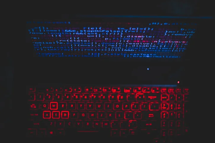 Dark-themed laptop setup with a red glowing keyboard and code on screen, ideal for tech enthusiasts.