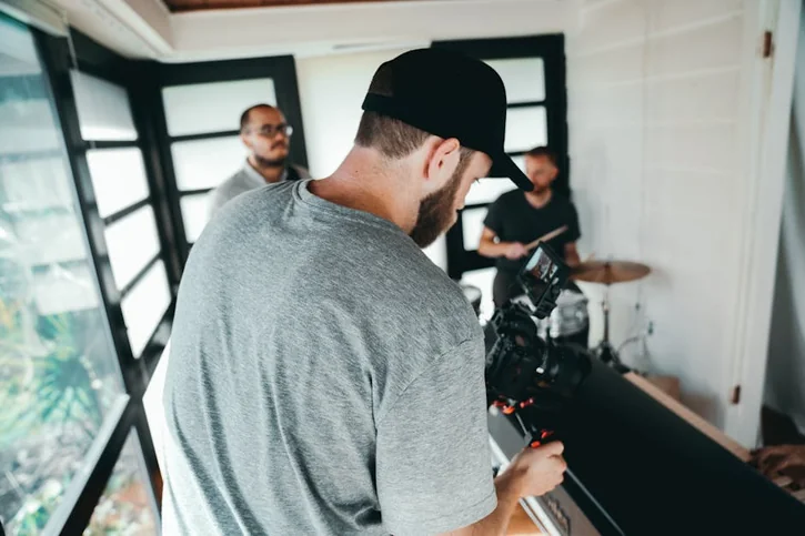 A filmmaker records a music session with drum beats indoors using professional gear.