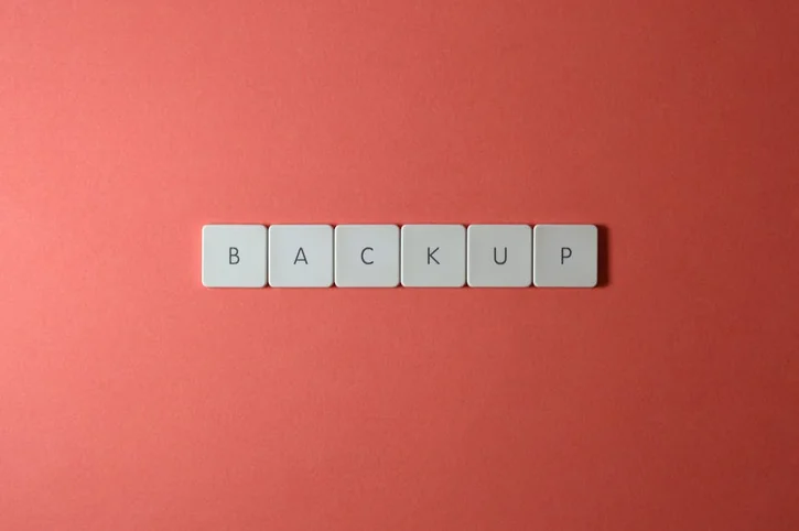 Close-up of keyboard keys spelling 'BACKUP' placed on a coral-colored surface.