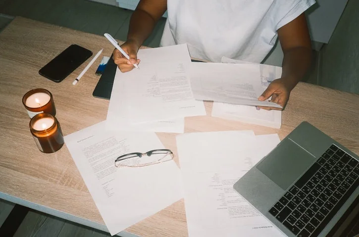 A person working at a desk with candles, documents, and a laptop, creating a cozy office atmosphere.