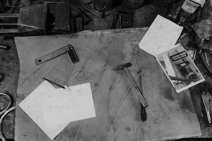 Black and white image of a blacksmith's workspace with tools and design sketches.