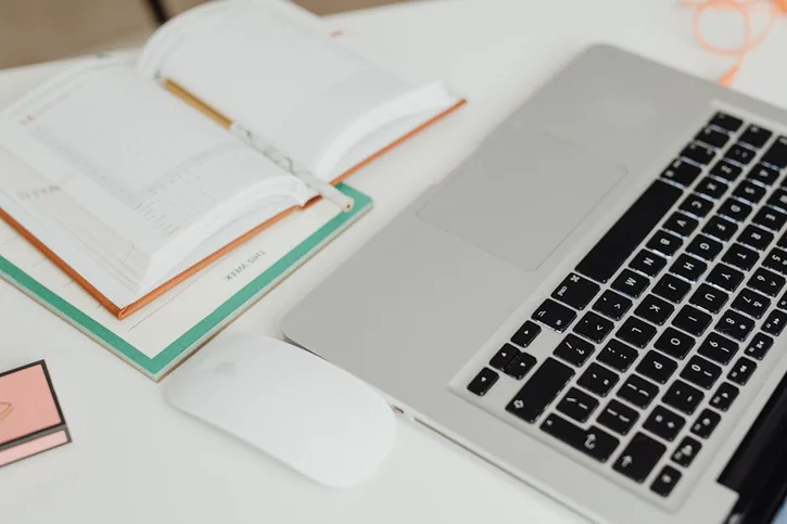 Overhead view of a modern workspace featuring an open planner and laptop on a tidy desk.