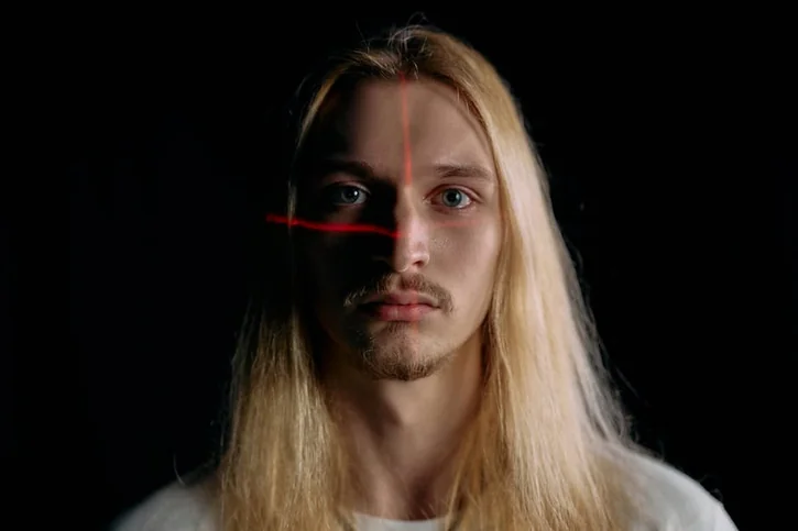 Close-up portrait of a man under laser scanning in low light, showcasing modern facial recognition technology.