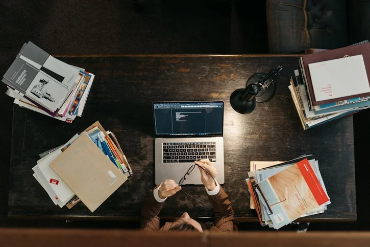 High-angle shot of a busy desk with books, laptop, and lamp, illustrating focused academia.