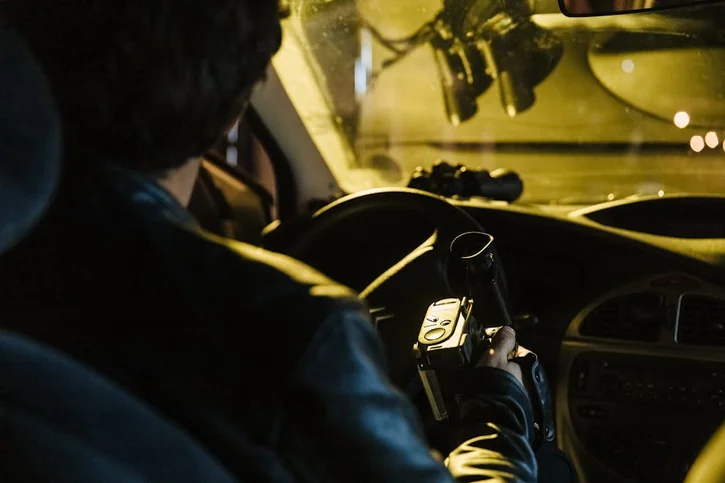 Back view of a man recording with a camcorder inside a car at night. Urban surveillance concept.