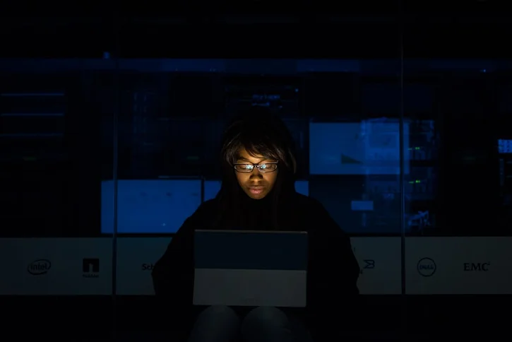 A woman deeply engrossed in programming on a laptop at night in a data center.