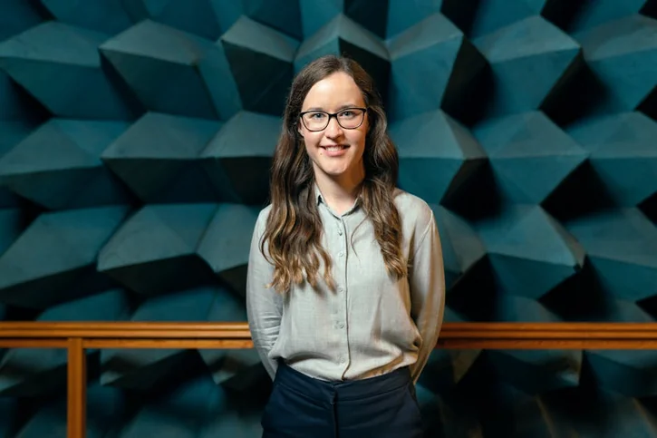 A smiling young professional in an acoustic room, showcasing engineering precision.