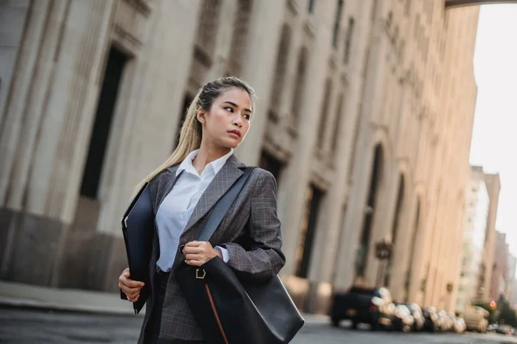 Professional woman in a suit confidently walking through urban cityscape with focus and determination.