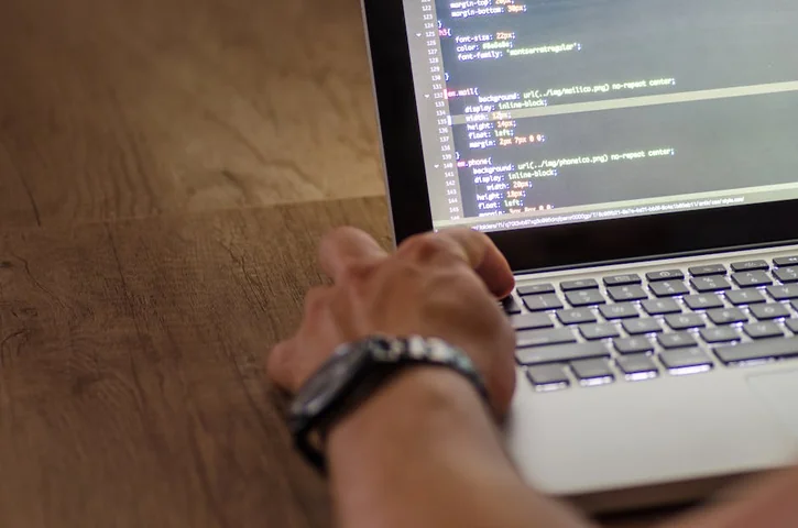 A developer's hand interacting with code on a laptop screen in a workspace setting.