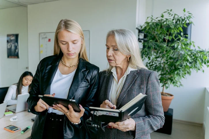 Professional women discussing work in a modern office setting with colleagues.