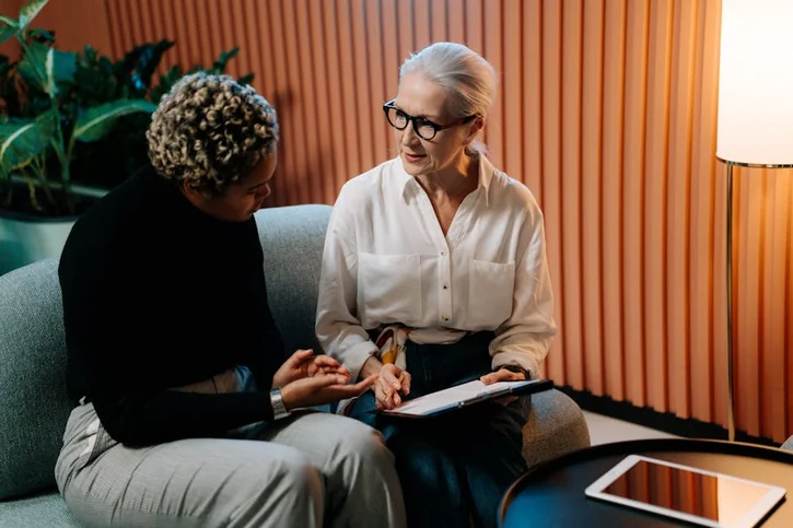 Two professional women engaged in a business discussion indoors with documents.