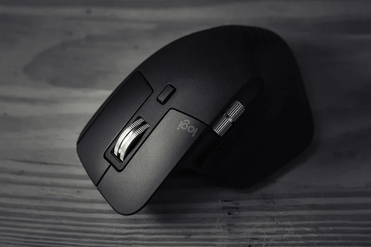 Close-up of a black ergonomic wireless mouse with metallic accents on a wooden background, highlighting modern design.