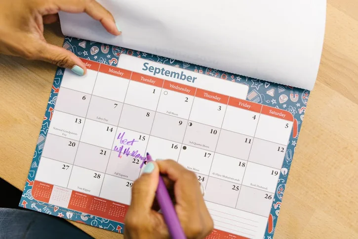 A person marking a calendar in September with a purple pen on a wooden desk.