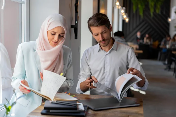 A man and woman study together with books in a bright, modern cafe setting.
