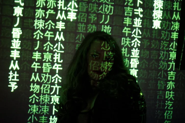 Silhouette of a woman with green code projected on her, depicting a tech and hacking theme.