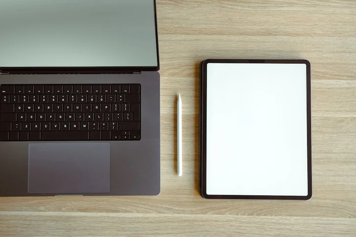 Top view of a sleek laptop and tablet setup on a wooden desk, ideal for tech workspaces.