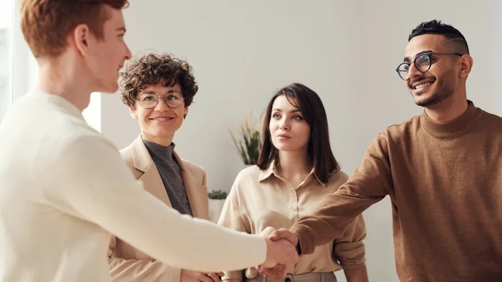 Four colleagues in an office handshake demonstrating teamwork and cooperation.