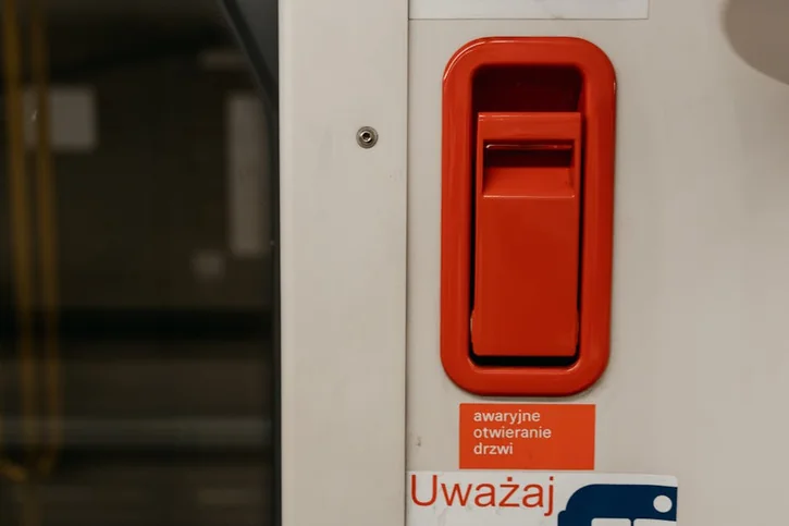 Close-up of a red emergency lever with Polish warning signs on a tram or train door.